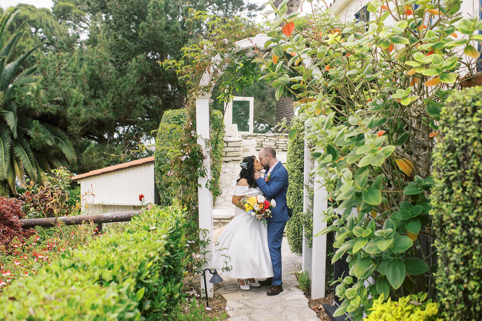 Bride and groom sharing a kiss beneath a blooming garden archway at La Venta Inn in Palos Verdes Estates, California.