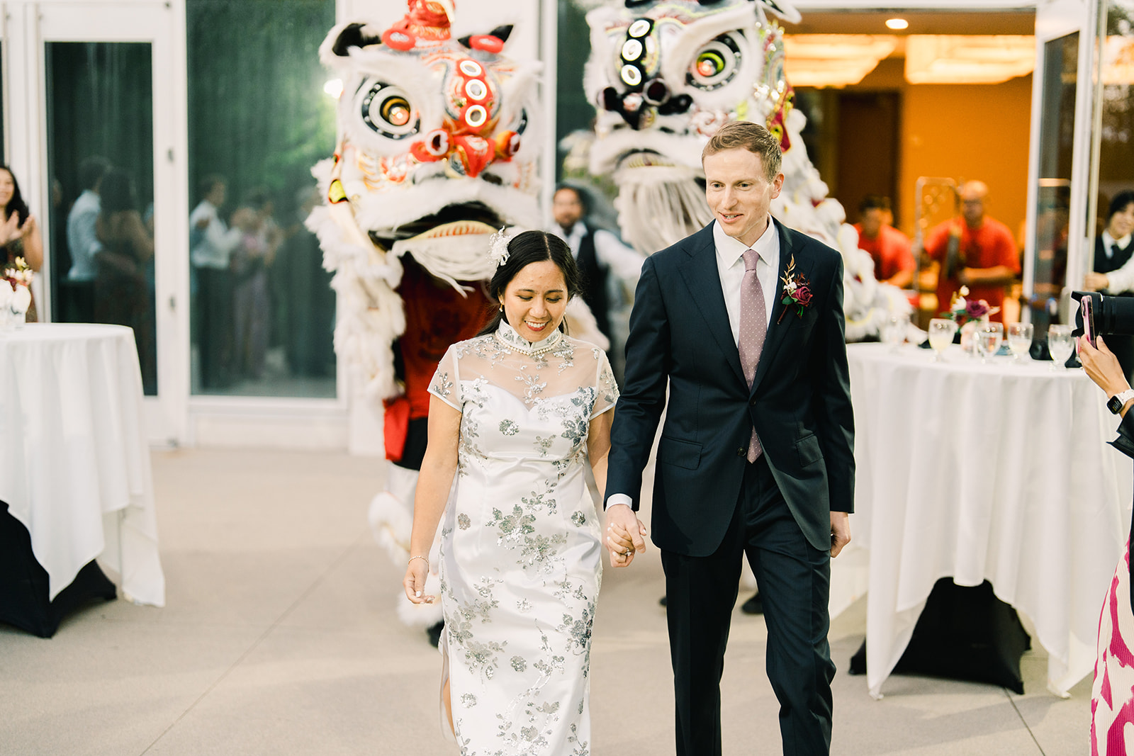 Bride and groom in elegant attire walking through a lively lion dance performance at a Miyako Hybrid Hotel wedding reception in Torrance, California.