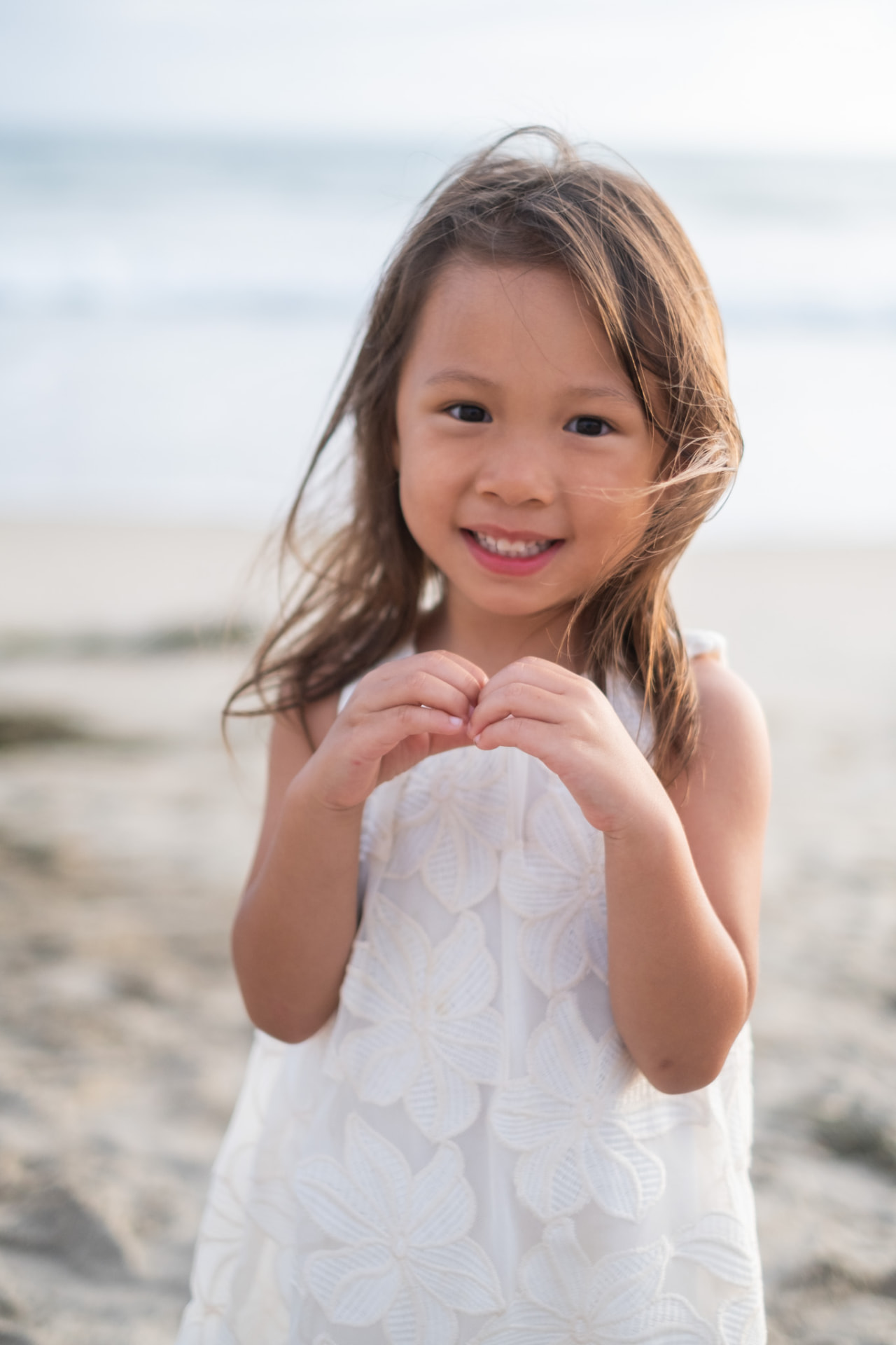 Little girl making a heart with her hands on the beach