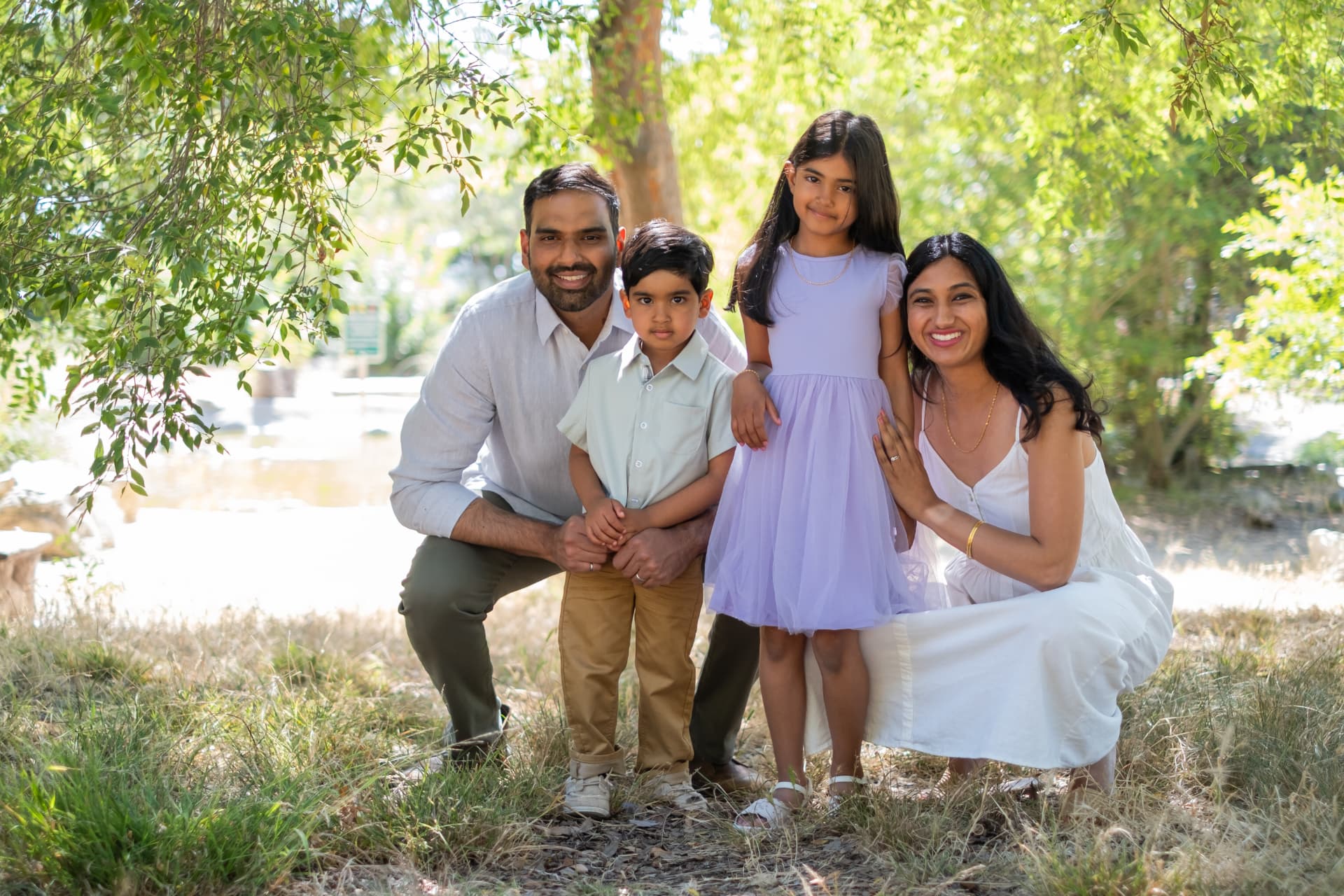 Family of four kneeling together in dappled light
