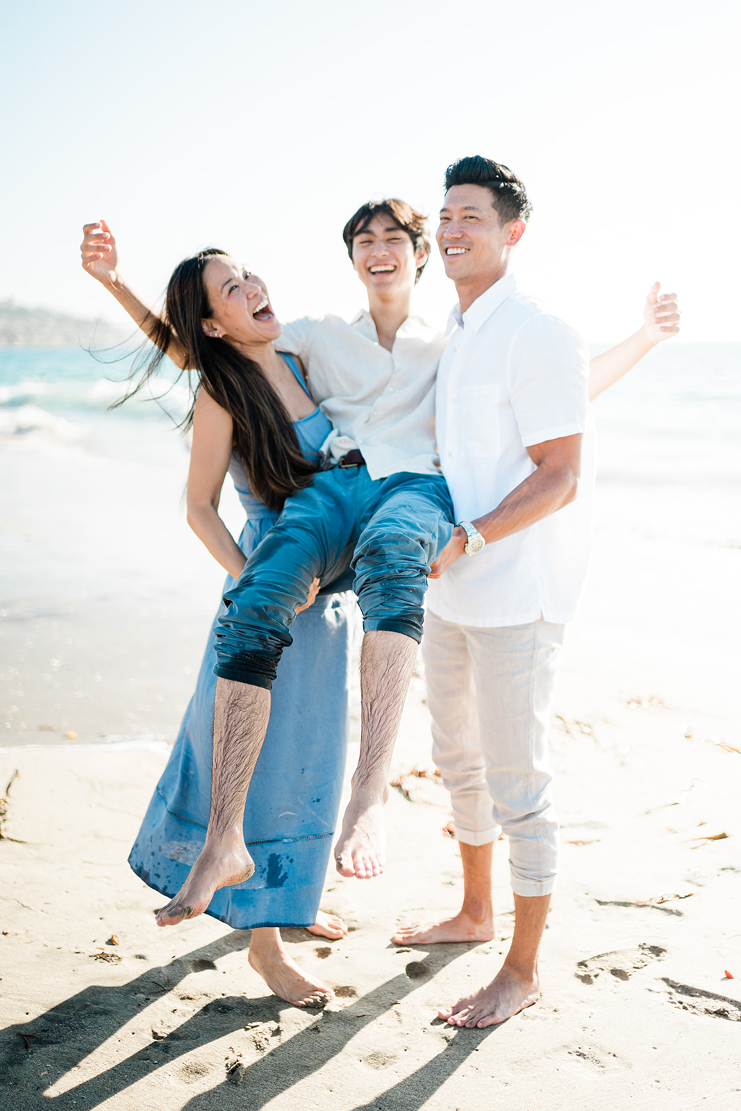 Parents carrying their laughing teenage son on the sand