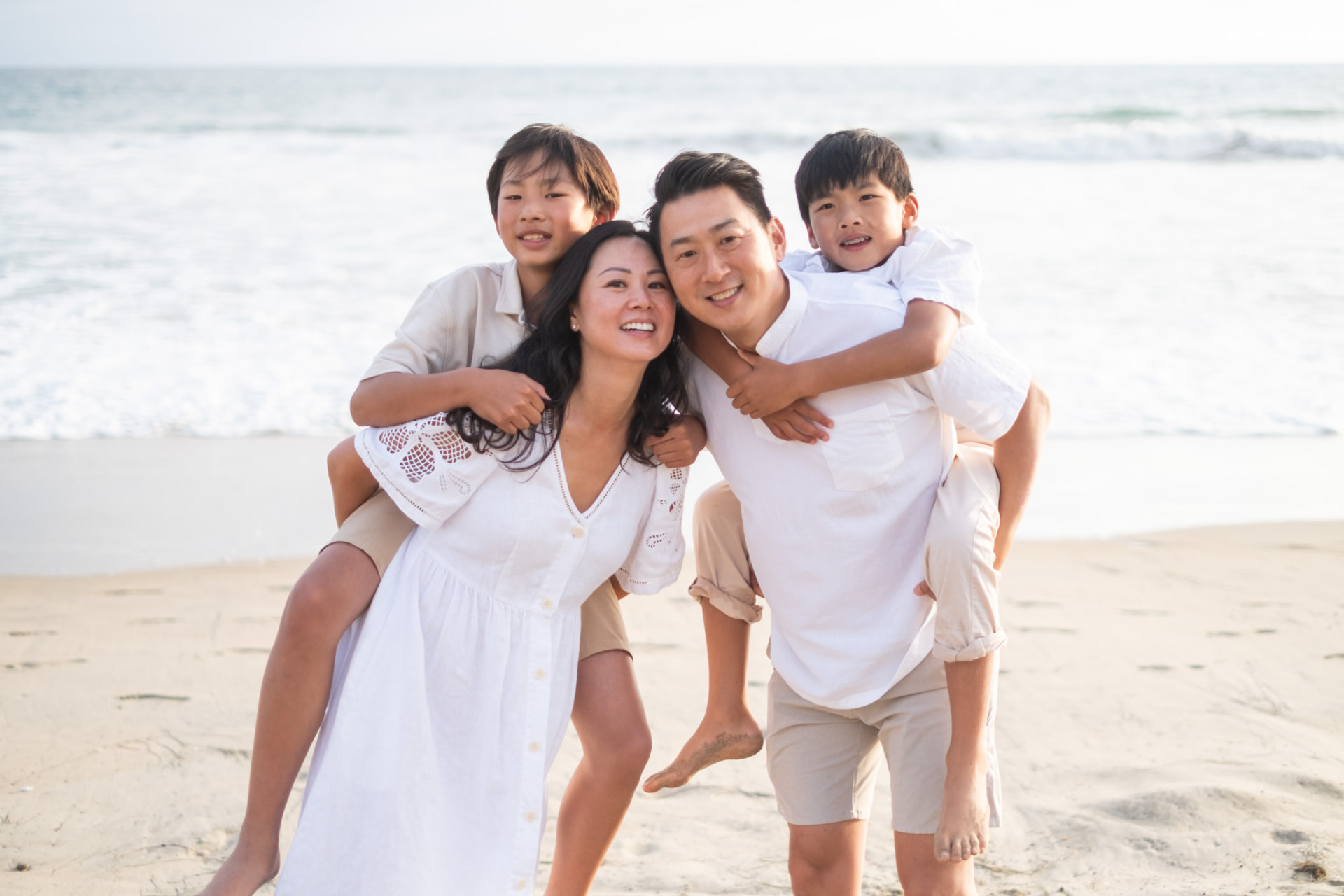 Parents giving their two sons piggyback rides by the waves