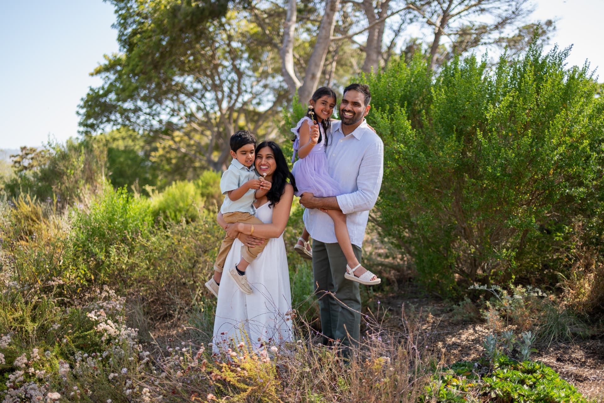 Family of four laughing together in a sunlit garden