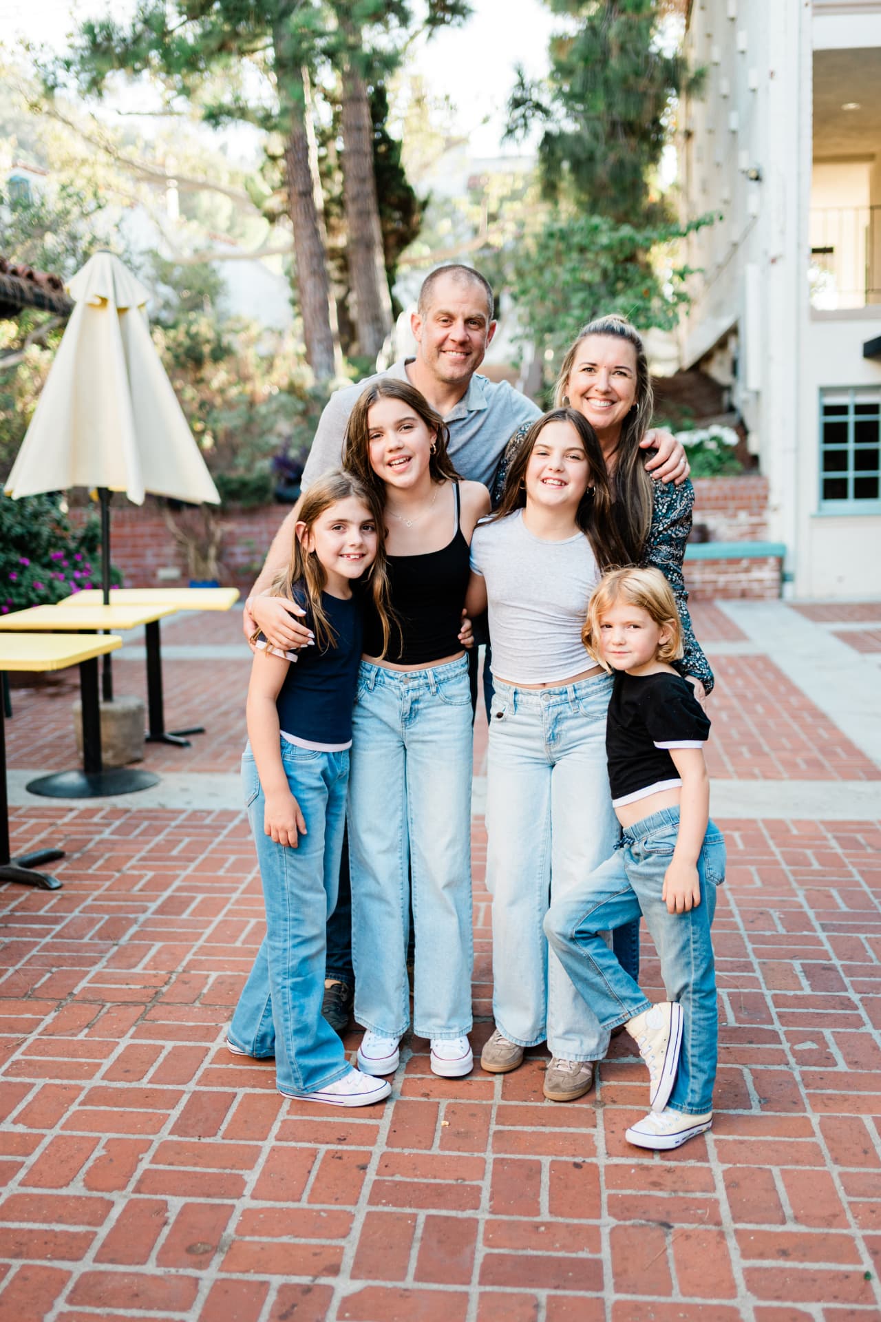 Family of six hugging together on a brick courtyard