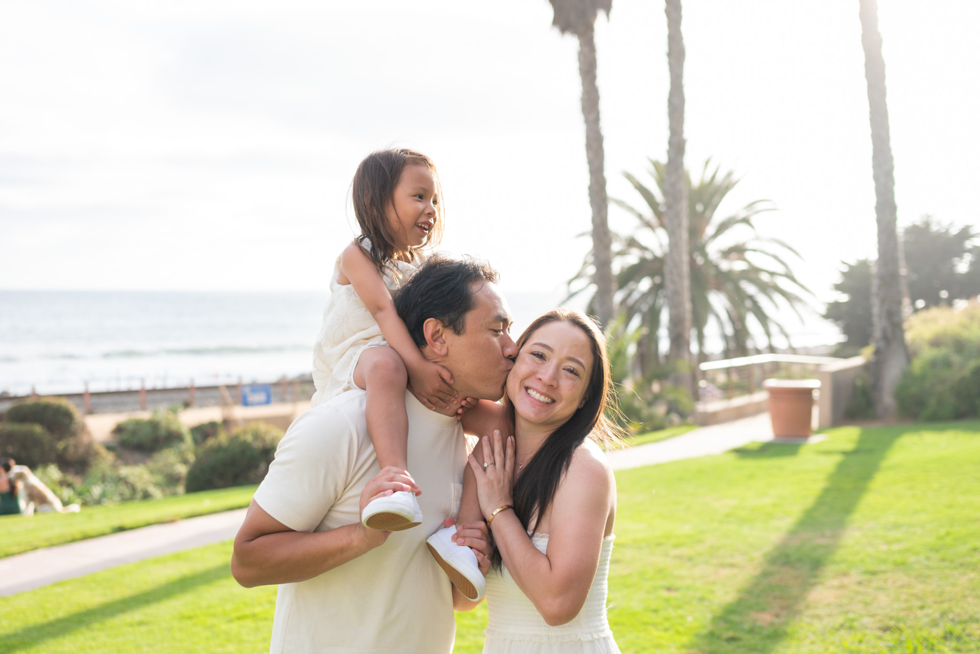 Dad kissing mom while their daughter rides his shoulders