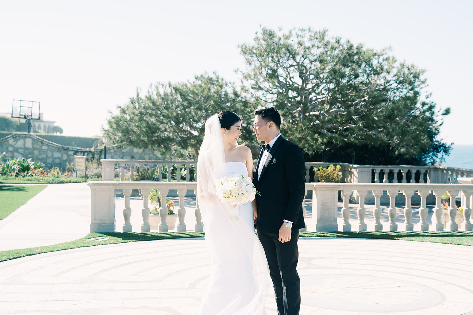 Bride and groom smiling at each other on the oceanfront stone terrace at Neighborhood Church in Palos Verdes Estates, California.