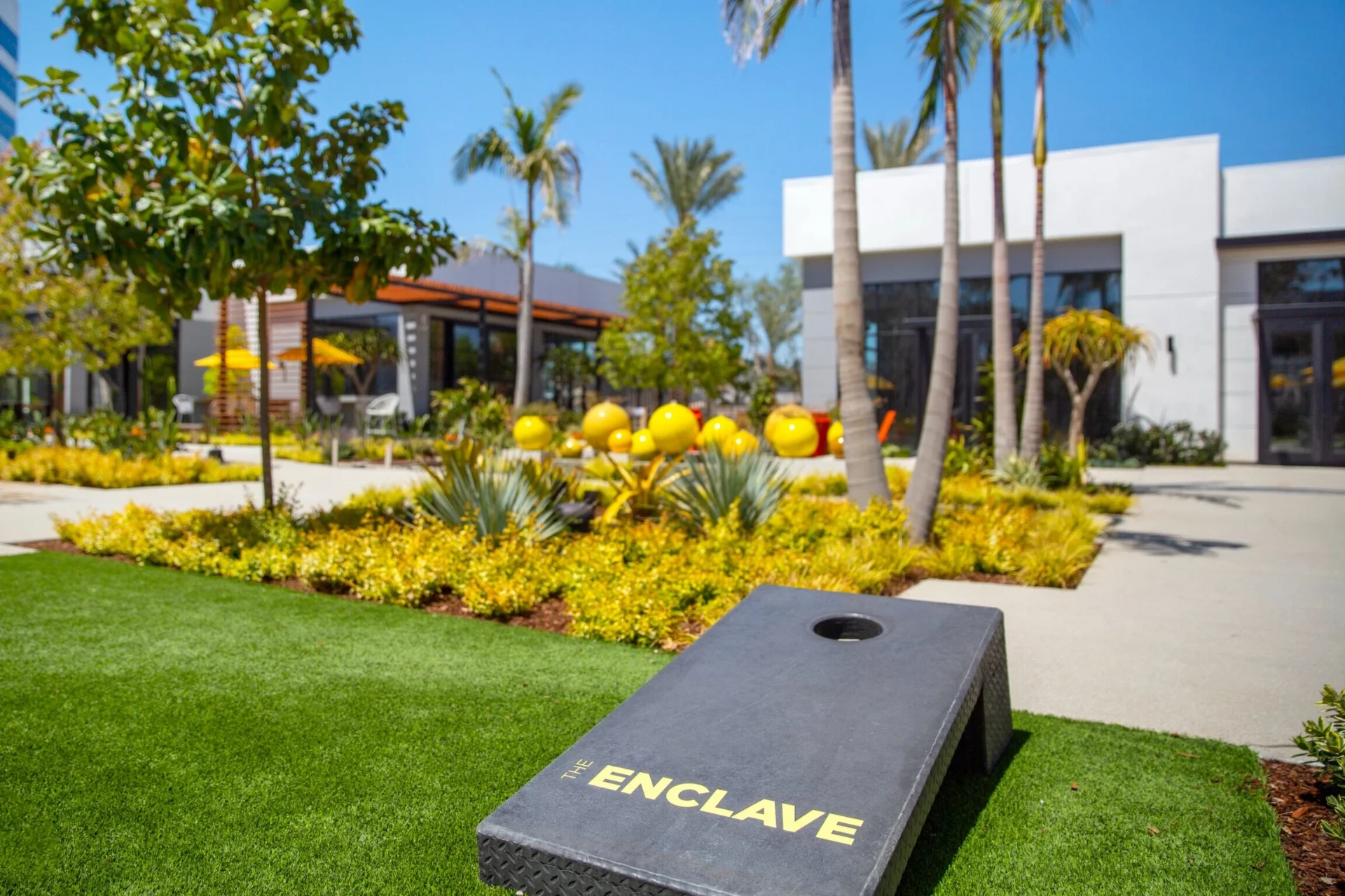 Sunny modern outdoor venue at The Enclave in Torrance, California, with palm trees, bright yellow landscaping accents, and contemporary white architecture.