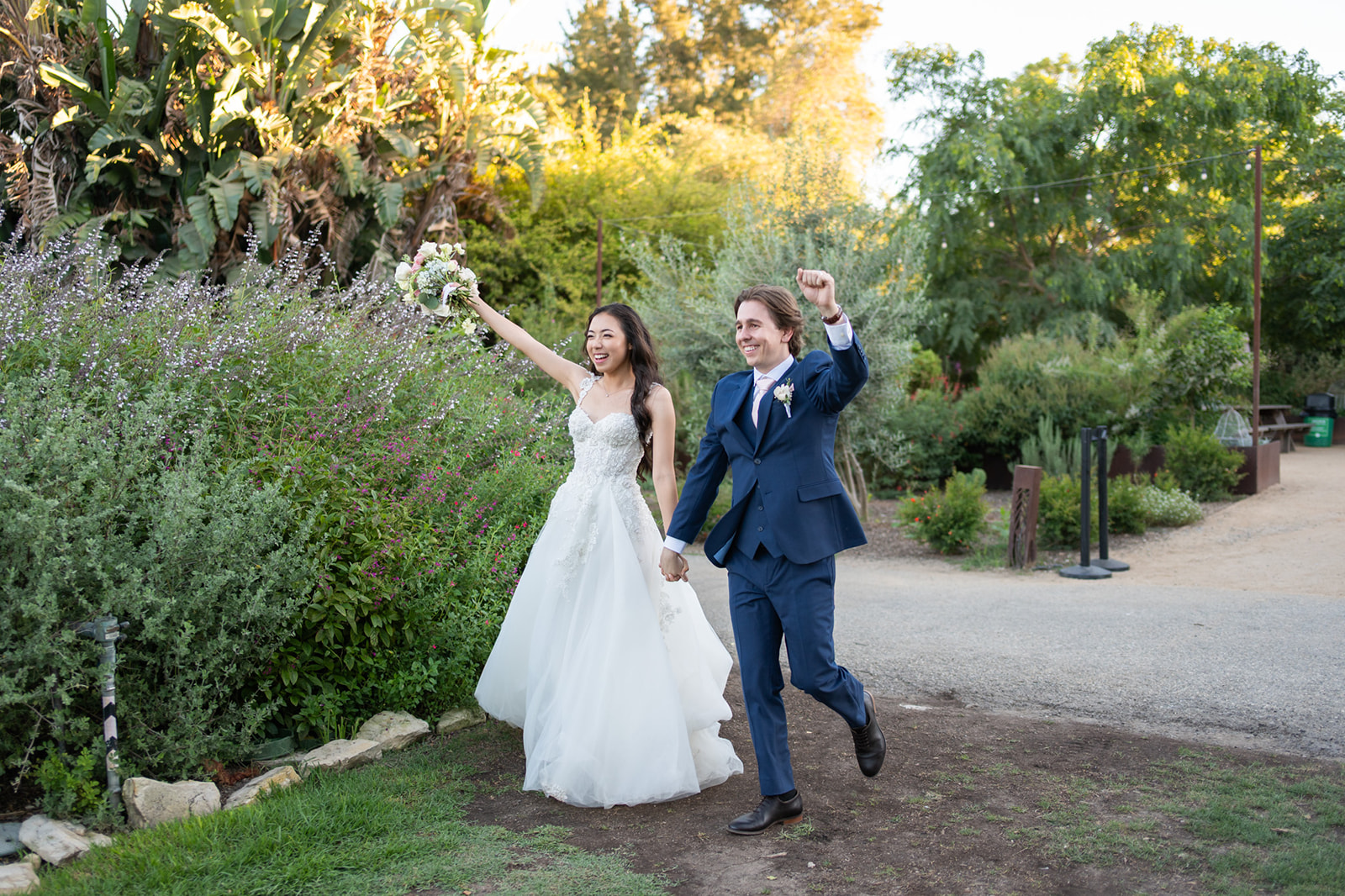 Bride and groom walking hand-in-hand through lush greenery and golden-hour light at South Coast Botanic Garden in Palos Verdes Peninsula, California.