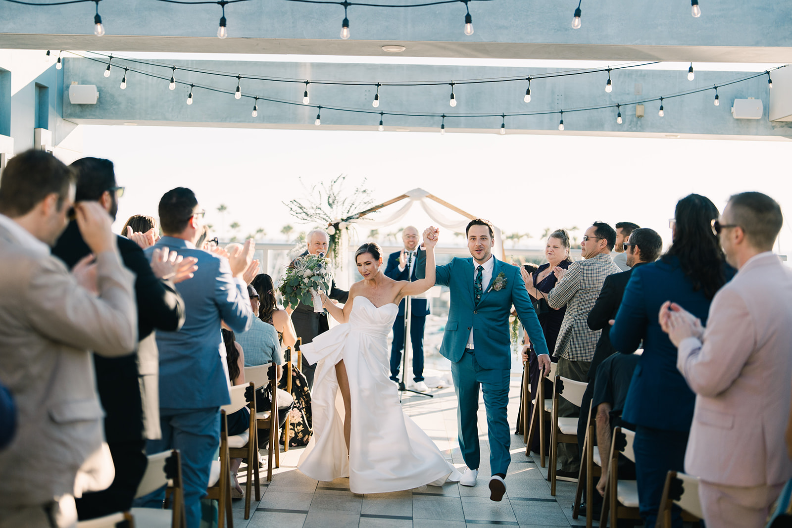 Bride and groom celebrating their recessional under string lights on the rooftop terrace at Shade Hotel Redondo Beach in Redondo Beach, California.
